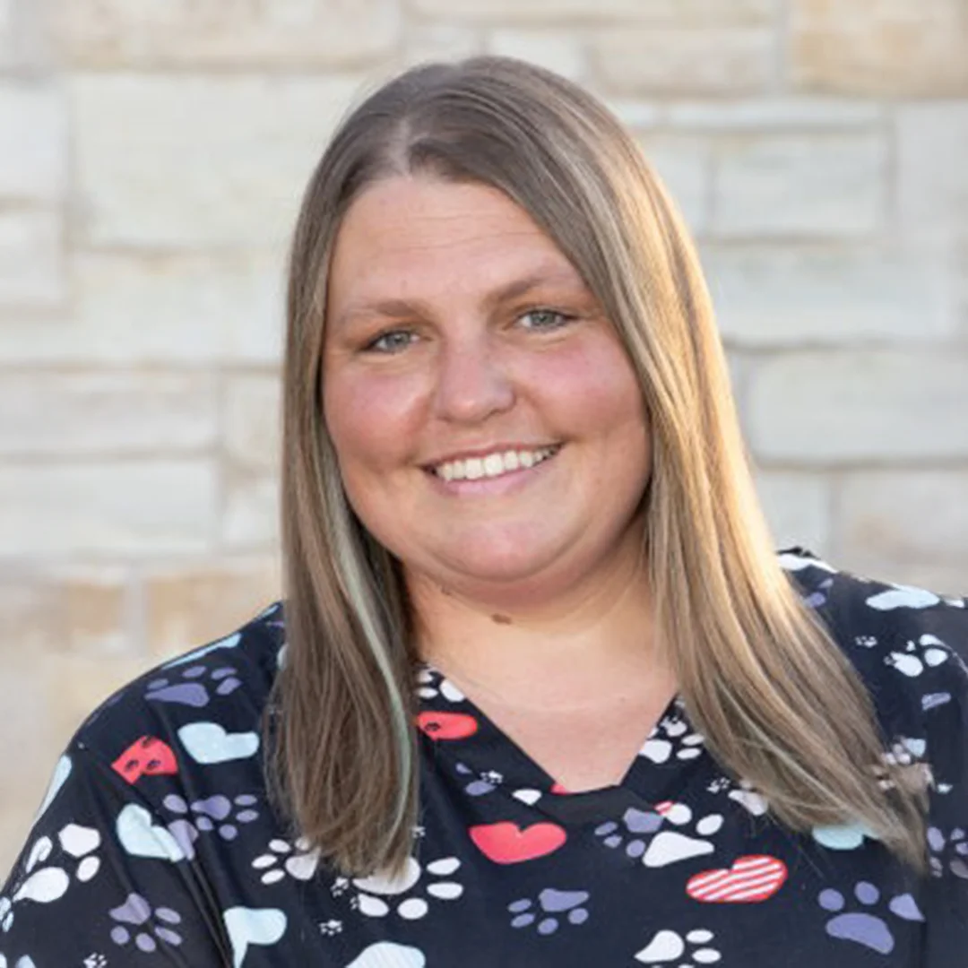 Woman with straight hair wearing paw-print scrubs smiling in front of a stone wall.