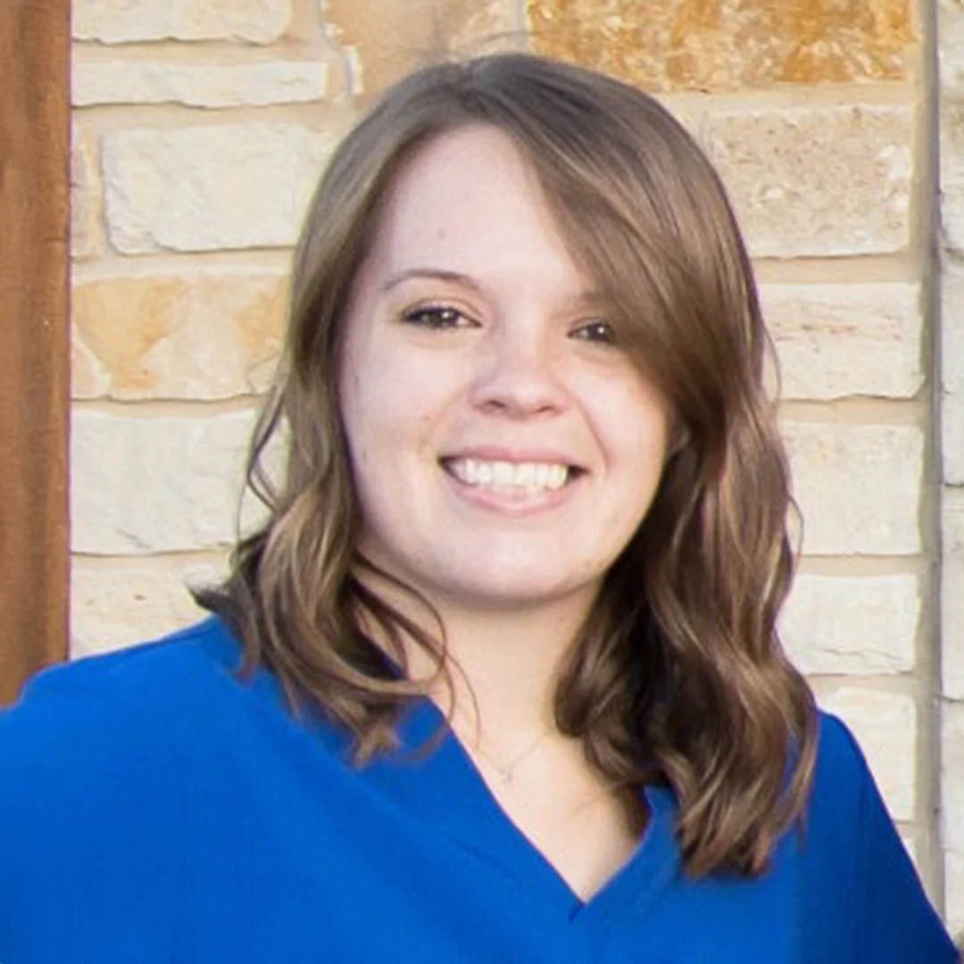 Woman with shoulder-length hair wearing a blue top smiling in front of a stone wall.